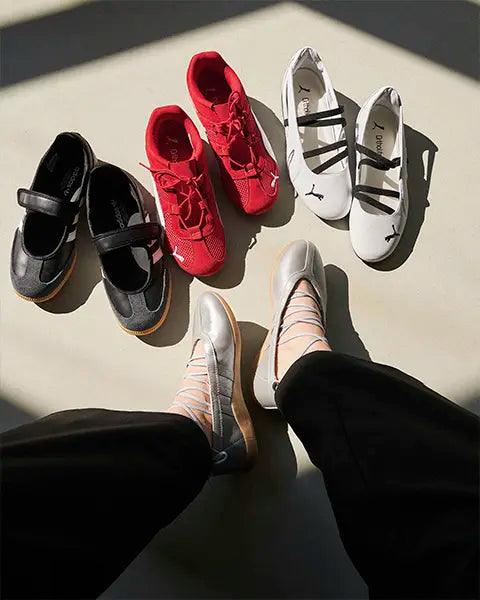 A pair of feet in silver shoes sits among four other shoes: two black, one red, and one white, arranged on a light surface. All models are Low Profile Sneakers as neaker trend 2025 2026 Puma Speedcat, adidas Ballet Sneaker, Samba Jane
